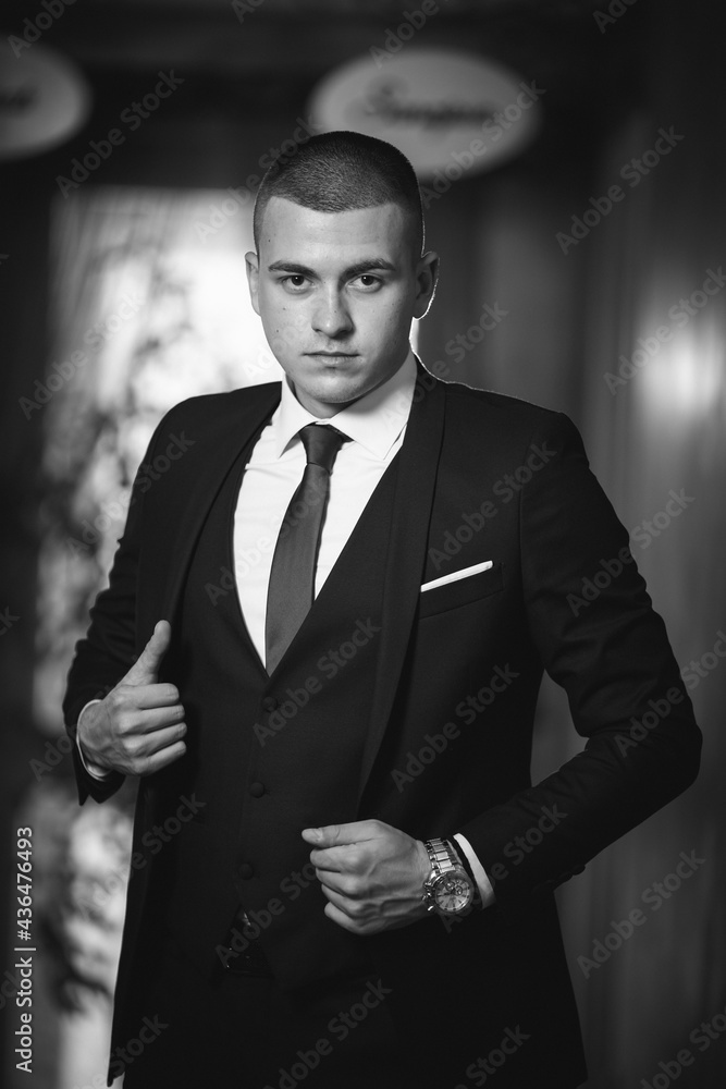 Wall mural Vertical shot of a white Caucasian man wearing a classic black suit and posing for a picture