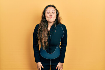 Young hispanic girl wearing diver neoprene uniform making fish face with lips, crazy and comical...