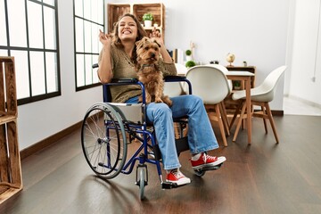 Young hispanic girl sitting on wheelchair at home with sad expression covering face with hands...