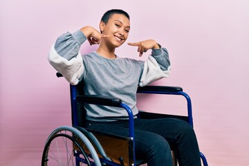 Beautiful hispanic woman with short hair sitting on wheelchair smiling cheerful showing and pointing with fingers teeth and mouth. dental health concept.