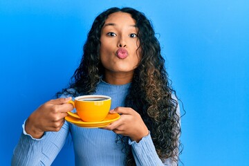 Young latin woman holding coffee looking at the camera blowing a kiss being lovely and sexy. love expression.