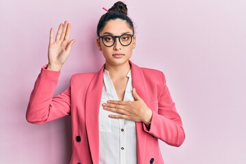 Beautiful middle eastern woman wearing business jacket and glasses swearing with hand on chest and...