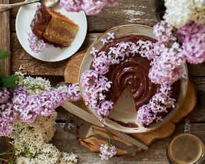 Chocolate cream cake decorated with lilac flowers. Top view, wooden and lilac background. 