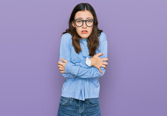 Young beautiful woman wearing casual clothes and glasses shaking and freezing for winter cold with...