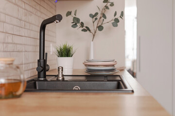 Obraz na płótnie Canvas Black kitchen sink made of artificial stone in a wooden home interior.