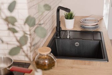 Black kitchen sink made of artificial stone in a wooden home interior.