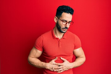 Young hispanic man wearing casual clothes and glasses with hand on stomach because indigestion,...