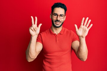 Naklejka premium Young hispanic man wearing casual clothes and glasses showing and pointing up with fingers number eight while smiling confident and happy.