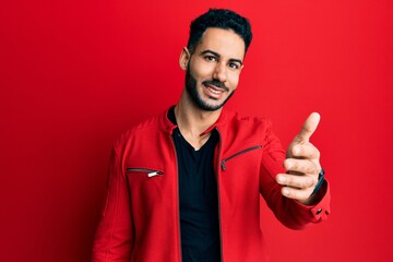 Fototapeta premium Young hispanic man wearing red leather jacket smiling friendly offering handshake as greeting and welcoming. successful business.