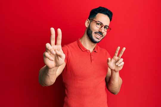 Young hispanic man wearing casual clothes and glasses smiling looking to the camera showing fingers doing victory sign. number two.