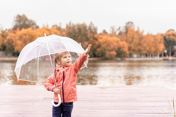 cute caucasian child girl with transparent umbrella having fun under the autumn rain
