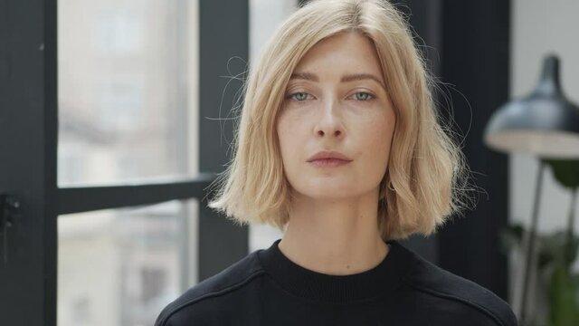 Blonde woman with a serious look, tense emotion. Attractive stylish adult person looking at the camera with neutral expression and pushing hair back behind. Concept of businesswoman