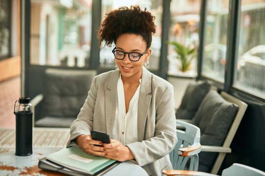 Young african american businesswoman smiling happy using smartphone sitting at coffee shop.