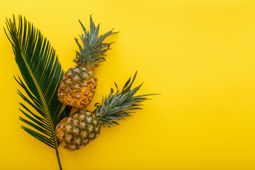 Pineapples and palm leaves on yellow color summer background. Tropical summer pineapples fruits flat lay composition with copy space