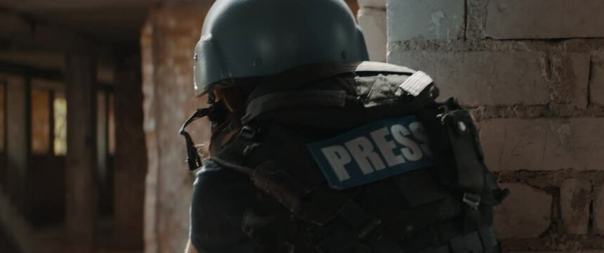 Caucasian female war journalist wearing protective helmet and bulletproof vest gear taking photos during military operation. Shot with 2x anamorphic lens