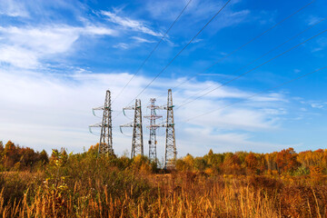 Power lines among autumn forest against blue sky.