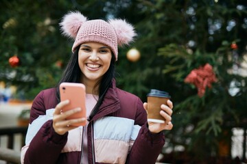 Young hispanic girl using smartphone and drinking coffee at the park.