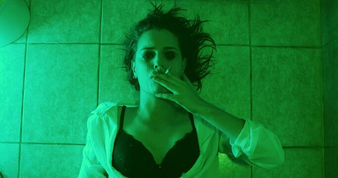 drugs, addiction - stoned young woman lying on the floor smokes a joint of weed