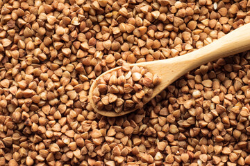 Obraz premium Buckwheat in a wooden spoon on the background of buckwheat