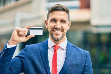 Young caucasian businessman smiling happy holding credit card at the city.