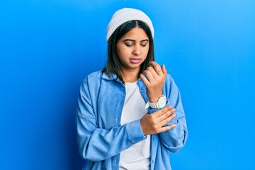 Young latin woman wearing cute wool cap suffering pain on hands and fingers, arthritis inflammation