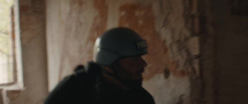 HANDHELD Portrait of Hispanic male war journalist wearing protective helmet and bulletproof vest gear taking photos during military operation. Shot with 2x anamorphic lens