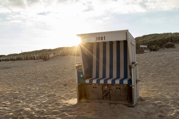 Sylt island beach landscape with empty beach chair and fine sand on the North Sea, at sunset. Sun star behind a beach chair. 