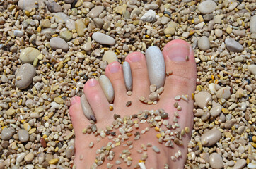 Children's small foot, fingers with pebbles on the background of a rocky beach on the seashore