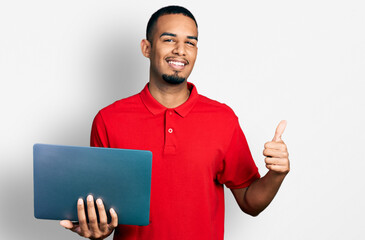 Young african american man working using computer laptop smiling happy and positive, thumb up doing excellent and approval sign