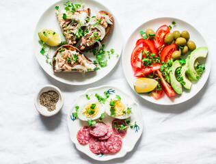 Snack, appetizers, tapas, breakfast table - salami, mackerel cream cheese sandwiches, olives, avocado, tomatoes, micro greens on a light background, top view
