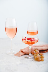 Rose wine in different types of glasses on light concrete background with grapes. Wine composition on white table. Vertical photo