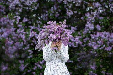 Beautiful woman in a dress covers her face with a purple bouquet of Lilacs. Girl holding large...