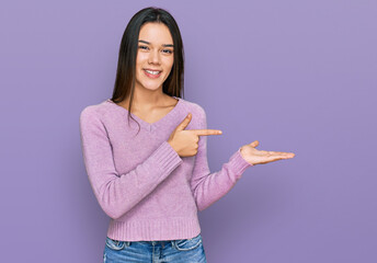 Young hispanic girl wearing casual clothes amazed and smiling to the camera while presenting with hand and pointing with finger.