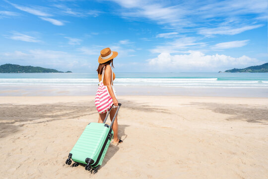 Young woman traveler with luggage relaxing and enjoying at beautiful tropical sand beach, Summer vacation and Travel concept