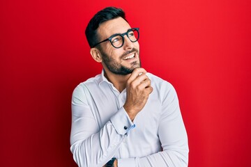 Young hispanic businessman wearing shirt and glasses with hand on chin thinking about question,...