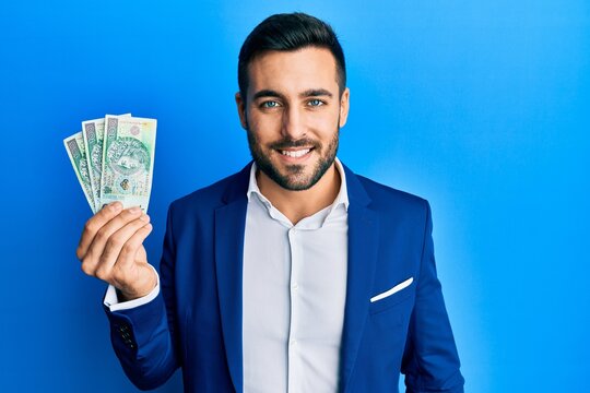 Young hispanic businessman wearing business suit holding polish zloty banknotes looking positive and happy standing and smiling with a confident smile showing teeth
