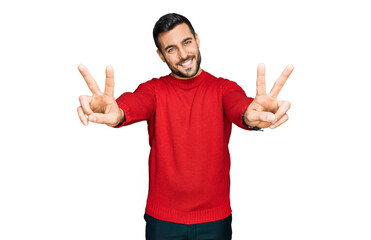 Naklejka premium Young hispanic man wearing casual clothes smiling with tongue out showing fingers of both hands doing victory sign. number two.