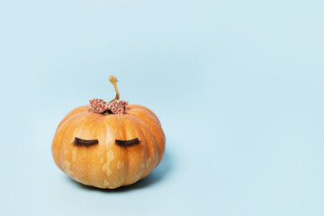 Pumpkin with false eyelashes and pink bow on blue background. Autumn, fall, halloween concept. copy space