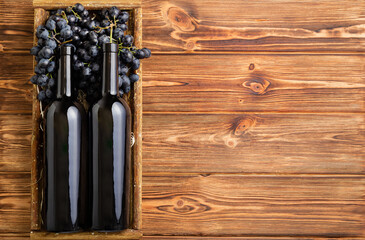 Two Red Wine bottles composition on brown wooden table. Red wine bottles in box on black ripe grapes on wooden table. Old collection wine label template Top view with copy space