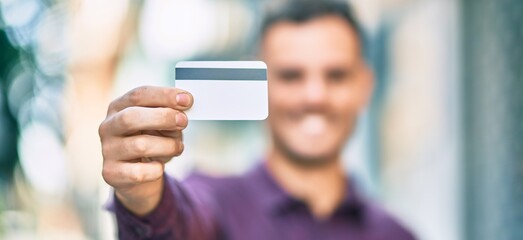Young hispanic man smiling happy holding credit card at the city.