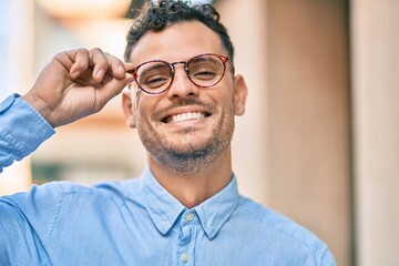 Young hispanic businessman smiling happy touching his glasses at the city.