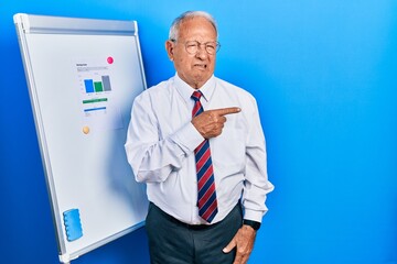 Senior man with grey hair standing by business blackboard pointing aside worried and nervous with...