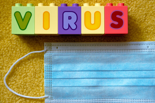The word "VIRUS" of colored cubes next to a medical face mask on a fluffy yellow surface