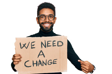 Young african american man holding we need a change banner smiling happy pointing with hand and...