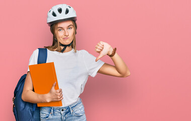 Beautiful young blonde woman wearing backpack and bike helmet with angry face, negative sign showing dislike with thumbs down, rejection concept