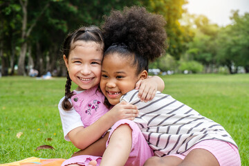Two African American cheerful little girl sitting on the mat and hugging each other with love in...