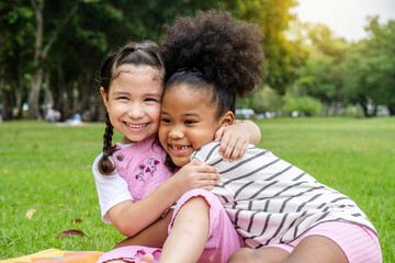 Two African American cheerful little girl sitting on the mat and hugging each other with love in the garden