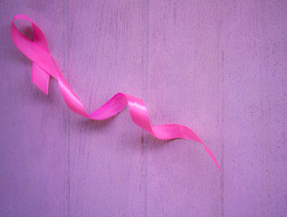 Pink breast cancer ribbon on white wooden table.