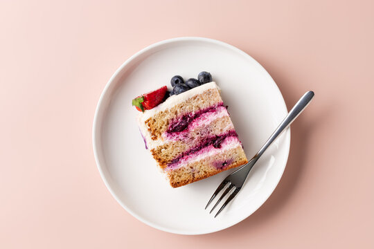 slice of blueberry cake decorated with fresh berries on white plate. delicious layered cake. pink background. top view