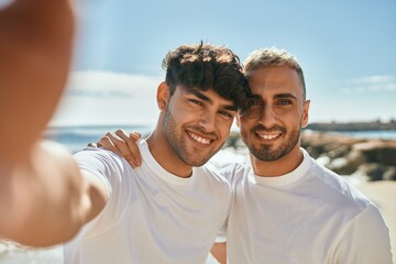 Young gay couple smiling happy making selfie by the smartphone at the beach.